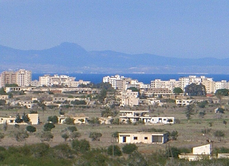 A coastal cityscape with buildings, a clear sky, and mountains in the distance. 5