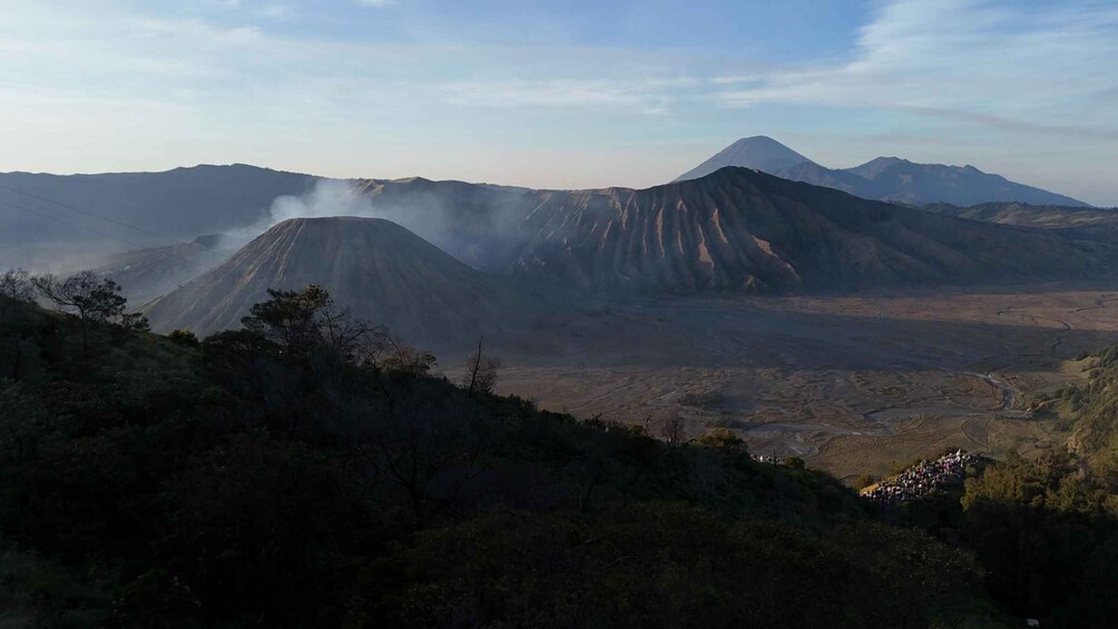 A volcanic landscape with multiple peaks, some emitting smoke, surrounded by forested hills. 4