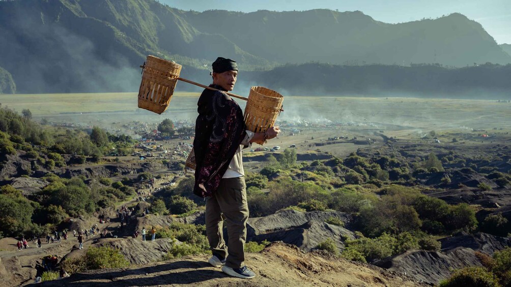 A person carrying baskets on a mountain with a valley in the background. 1