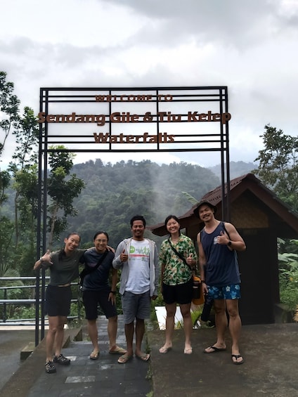 A group of people standing in front of a sign that reads 'Welcome to Sendang Gile & Tiu Ketep Waterfalls.' 1