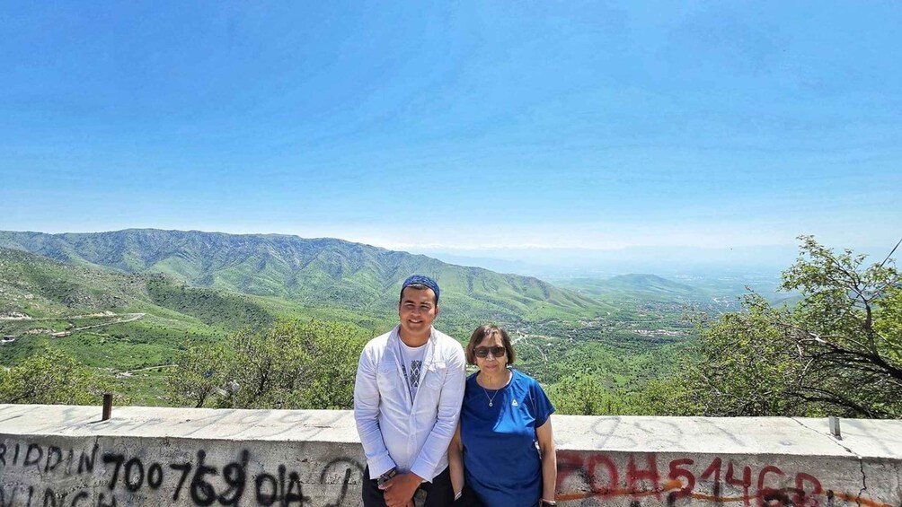 Two people standing on a concrete ledge with graffiti, overlooking a mountainous landscape. 4