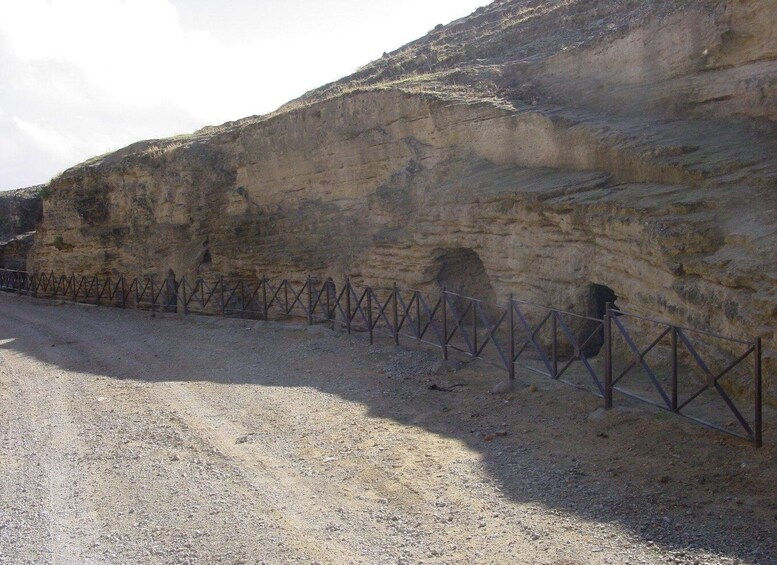 A rocky cliff with a metal fence and a dirt road. 5