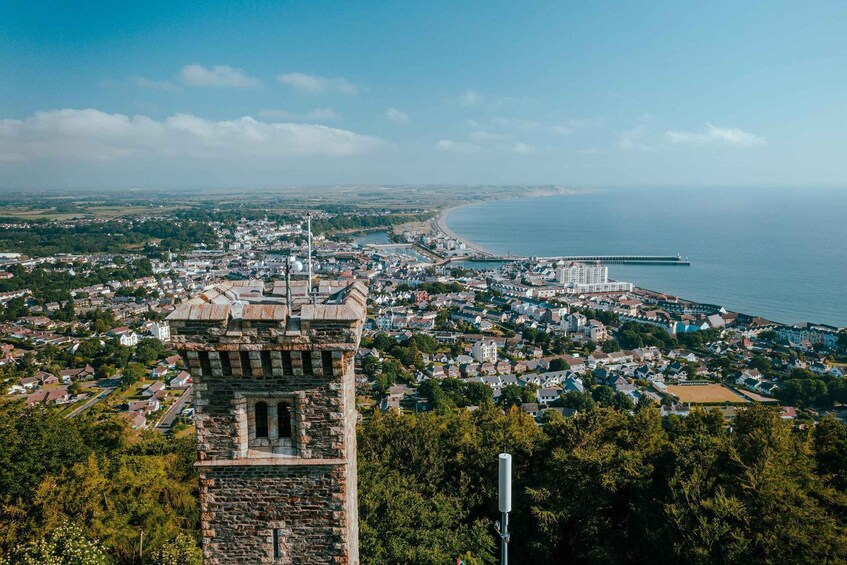 A coastal cityscape with a prominent stone tower, a beach, and a distant ship. 2