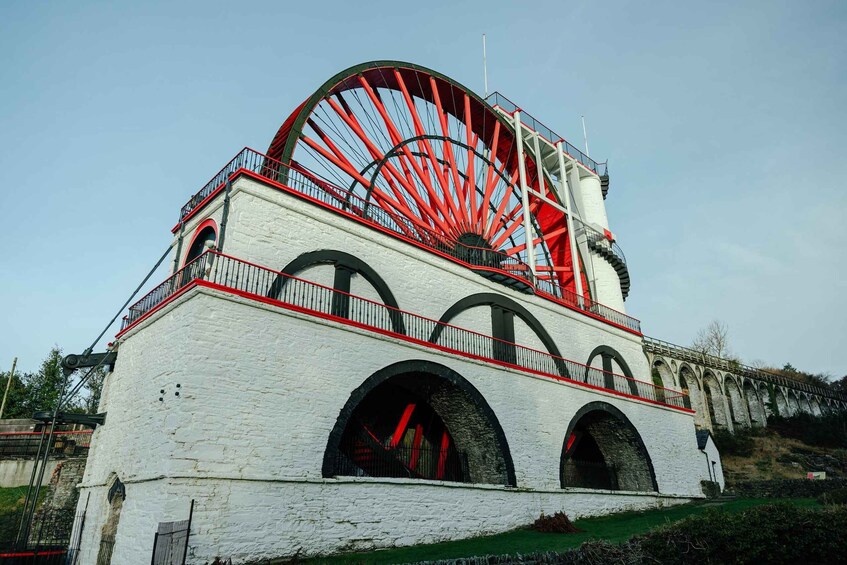 A large water wheel attached to a white building with red accents and arched windows. 3