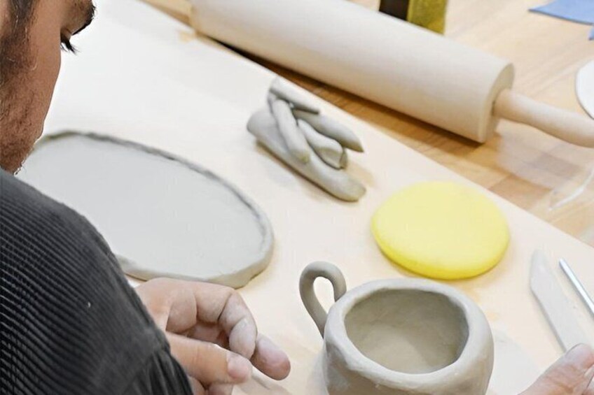 A person working with clay on a table, surrounded by pottery tools and a rolling pin. 3