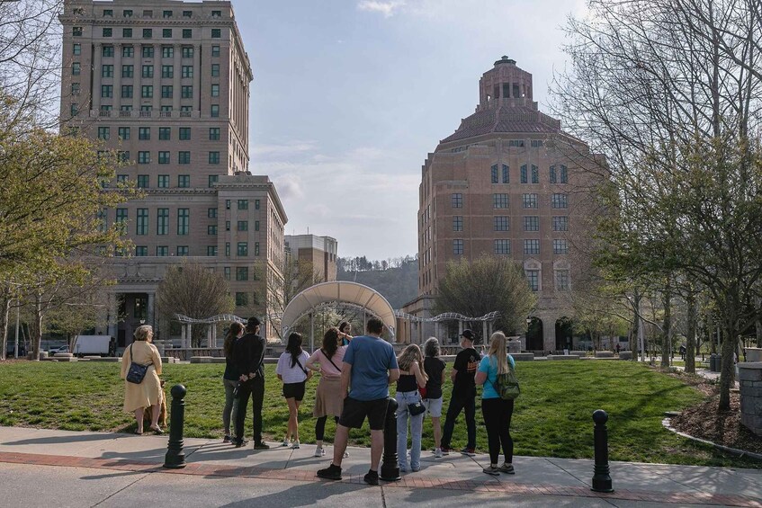 A group of people standing on a grassy area in front of a large building with a distinctive tower. 2