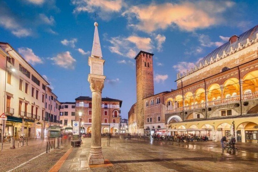 A historic square with a prominent tower, a central monument, and surrounding buildings with arches. 5