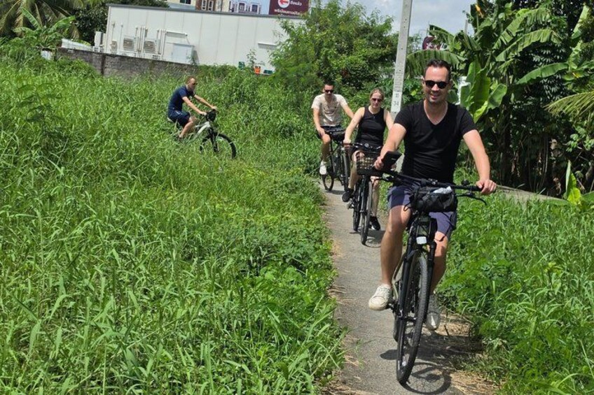 A group of cyclists on a narrow path surrounded by lush greenery. 3