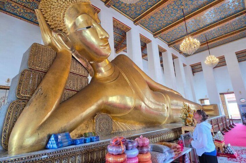 A large golden reclining Buddha statue in a temple with intricate ceiling designs and a person standing nearby. 1