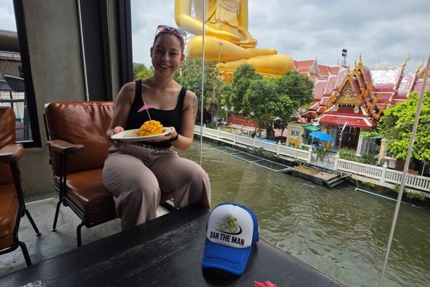 A person sitting by a window with a view of a river, a large yellow statue, and traditional architecture. 2