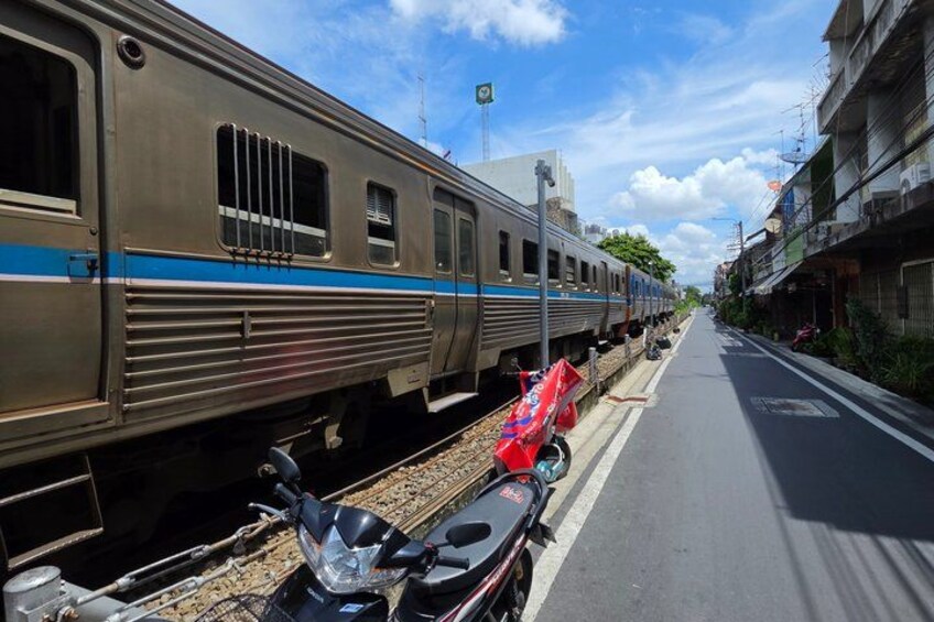 A train on tracks with a blue stripe, a motorcycle, and buildings along the street. 4