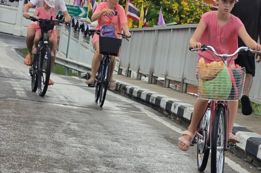Three people riding bicycles on a wet road with a metal guardrail and a concrete barrier. 3