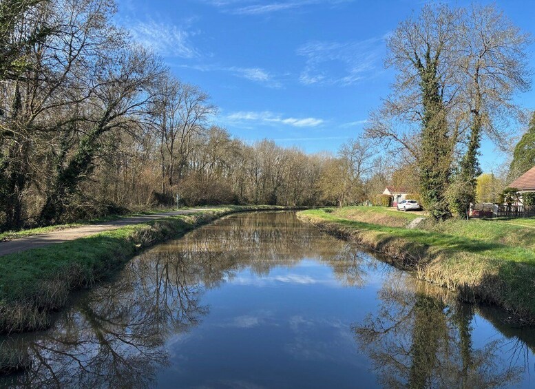 A calm river with trees reflecting in the water, a pathway, and a house in the background. 4