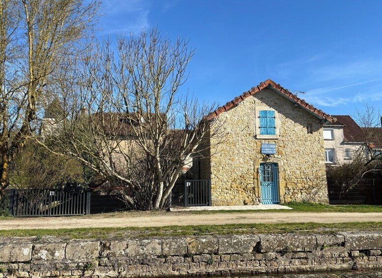 A stone building with a blue door and window shutters, surrounded by trees and a stone wall. 5