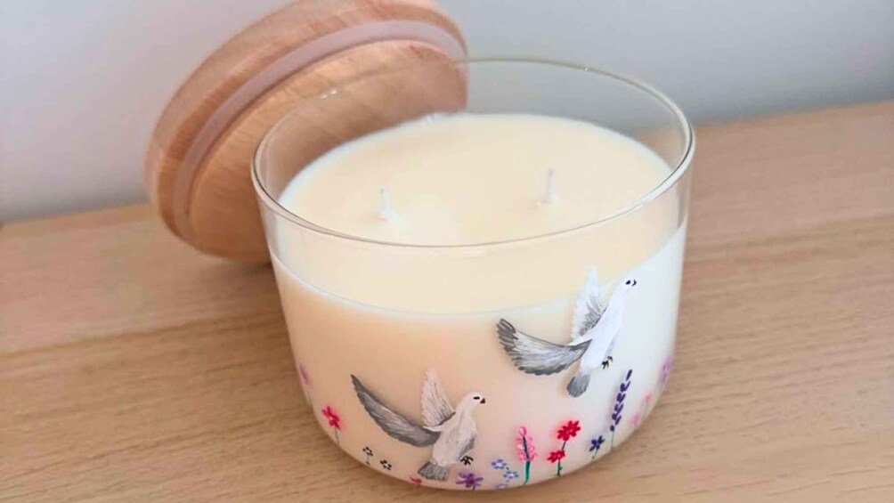 A candle with a wooden lid and a glass container, featuring painted birds and flowers. 1
