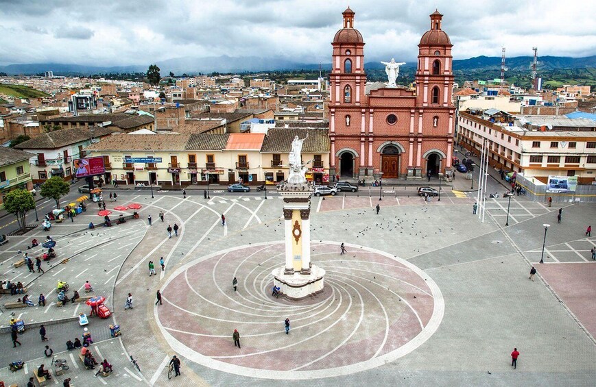 A plaza with a central monument, a church with two domes, and surrounding buildings. 4