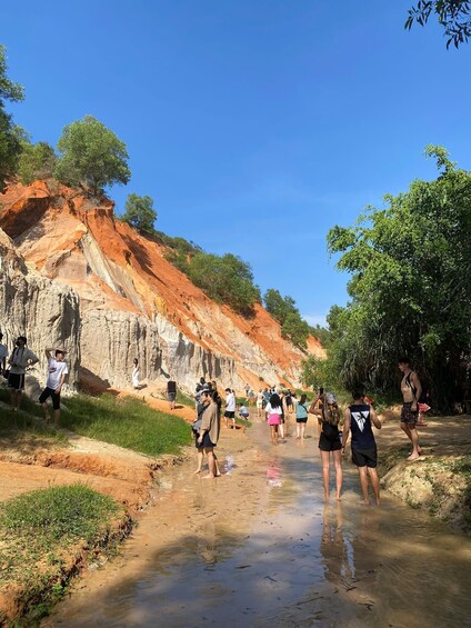 A group of people walking along a riverbank with red cliffs and greenery. 2
