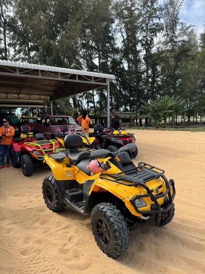 A group of off-road vehicles parked in a sandy area with a shelter and trees in the background. 3