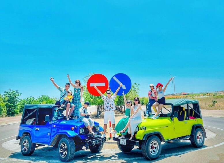 A group of people posing with a blue and a yellow off-road vehicle in a parking lot with a clear blue sky. 1