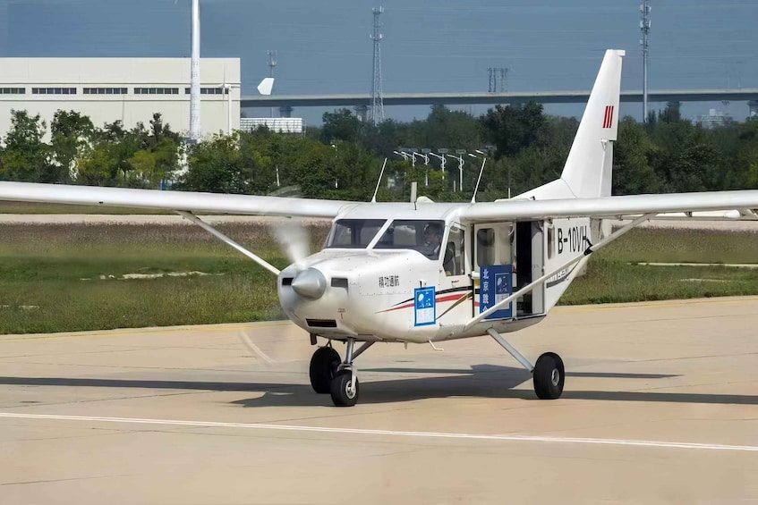 A small white airplane on a runway with a bridge and industrial buildings in the background. 2
