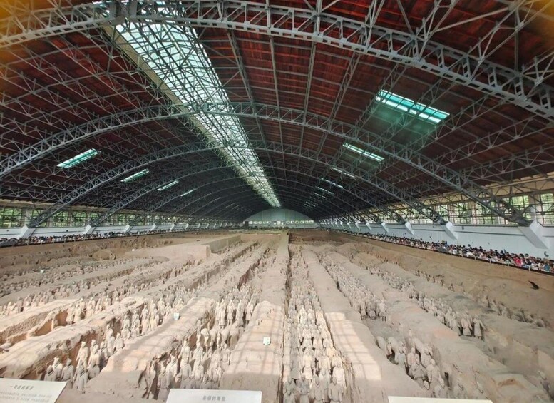 A large indoor exhibition hall with a high ceiling and a central display of numerous terracotta soldier statues. 1