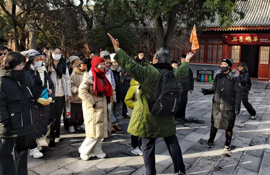 A group of people outdoors, some wearing winter clothing, gathered around a person holding an orange flag. 3