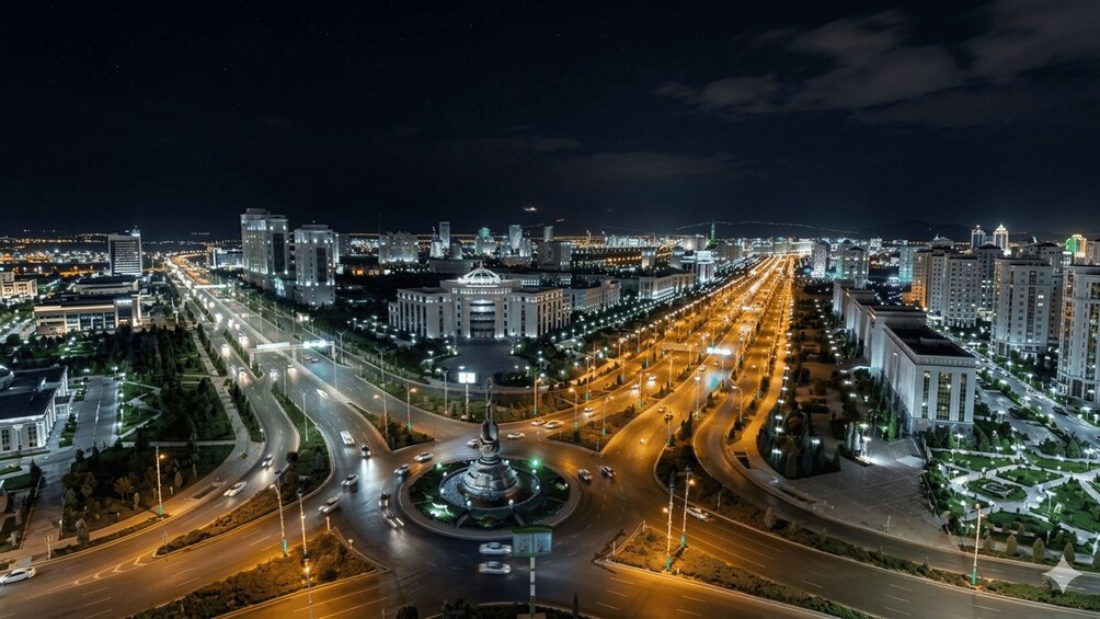 A nighttime cityscape with a central roundabout, illuminated buildings, and a long stretch of road. 1