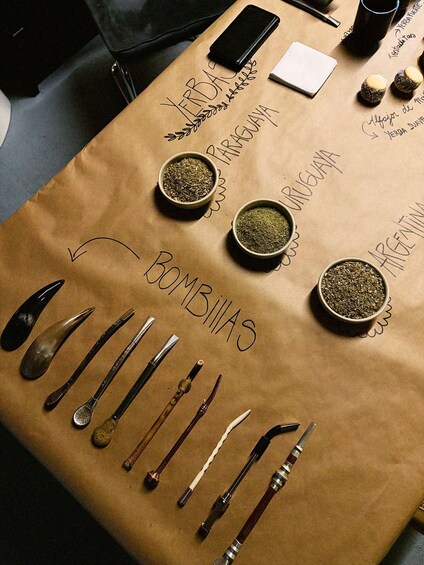 A table with a paper bag labeled 'BOMBILIAS,' containing various utensils and two small bowls of what appears to be tea. 1