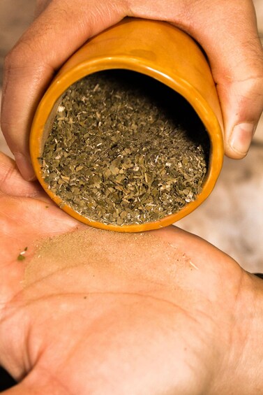 A hand holding a small, orange ceramic bowl filled with dried herbs. 5