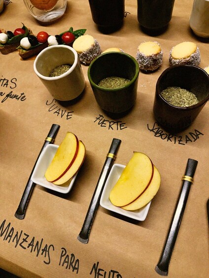 A table with food items and utensils, including sliced apples, a knife, and bowls of herbs. 4