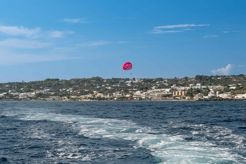 A body of water with waves, a distant shoreline with buildings, and a pink parachute-like object in the sky. 2