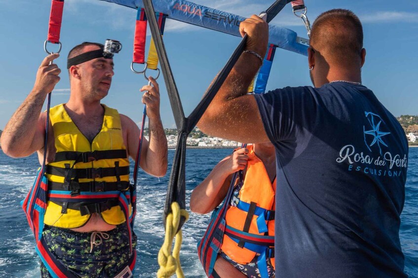 Two people on a boat, one wearing a yellow life jacket and the other in a blue shirt, with ropes and a camera visible. 3