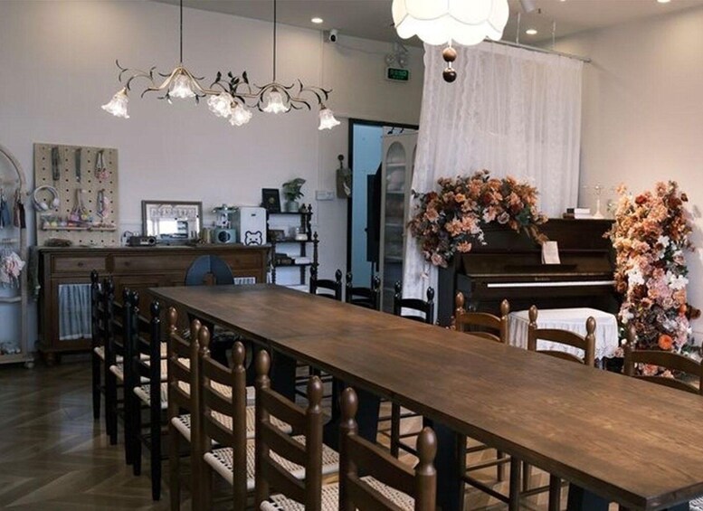 A dining area with a long wooden table, chairs, a piano, and a floral arrangement. 5
