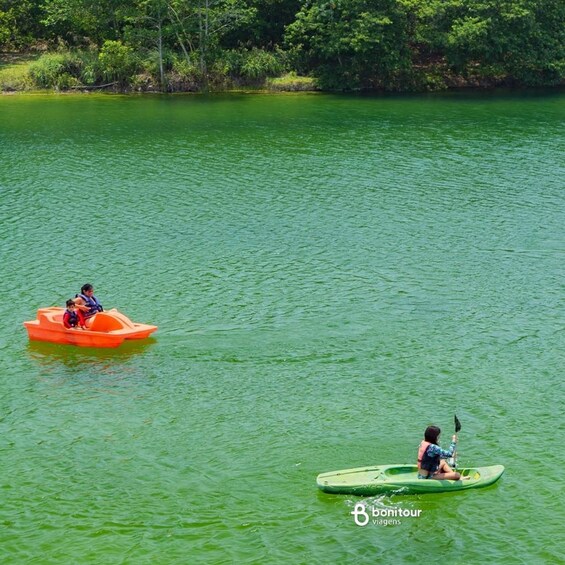 Two people kayaking on a green river surrounded by trees. 4
