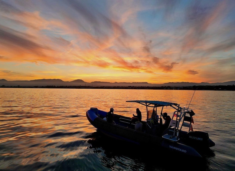 A boat named 'VANGUARD' on calm water during sunset with a colorful sky. 1