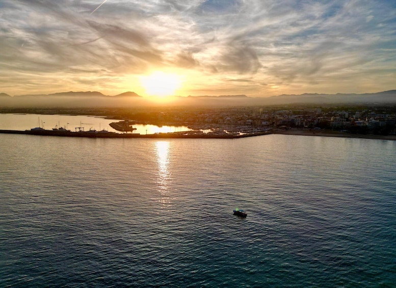A sunset over a calm sea with a distant shoreline and a small boat. 2