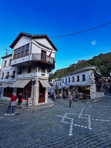 A cobblestone street with historic buildings, a balcony with a red flag, and a sign that reads 'OLD WELL INSIDE.' 1