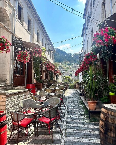 A cobblestone street with outdoor seating, hanging flowers, and buildings with signage. 5