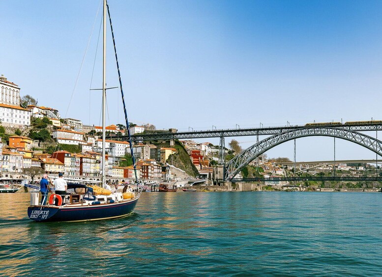 A sailboat named 'LIBERTÉ' on calm waters, a bridge, and a densely built hillside town. 4