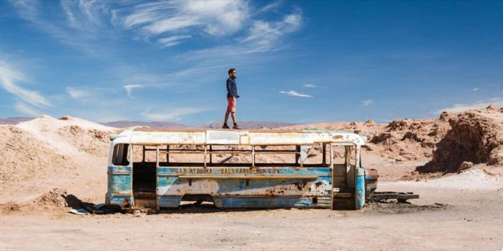 A person standing on a rusted bus in a desert landscape. 1