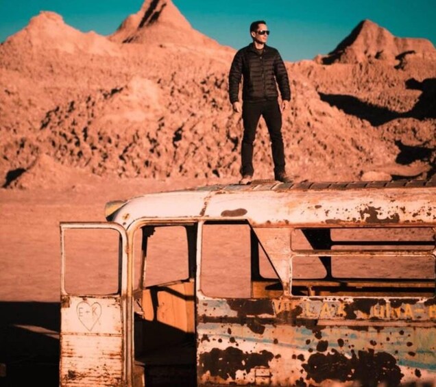A person standing on a rusted vehicle with a desert landscape in the background. 4