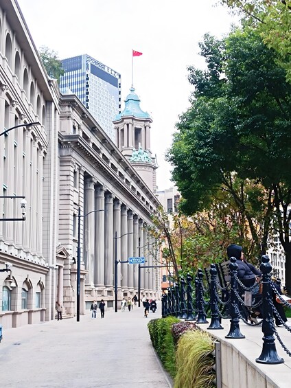 A city street with classical architecture, a flag on a tower, and a pedestrian walkway. 3