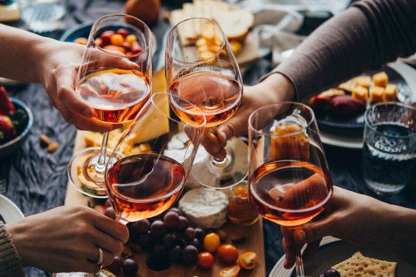 People toasting with wine glasses, cheese, and grapes on a table. 2