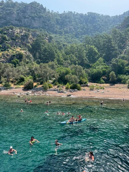 People swimming and kayaking in a clear lake surrounded by forested hills. 3