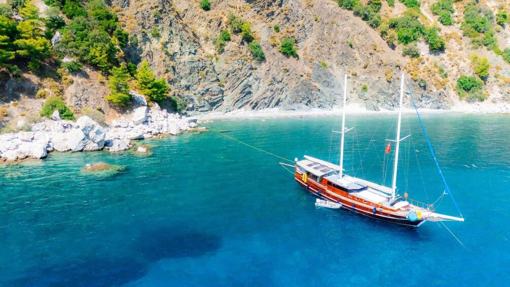 A sailboat anchored near a rocky coastline with clear turquoise waters. 2