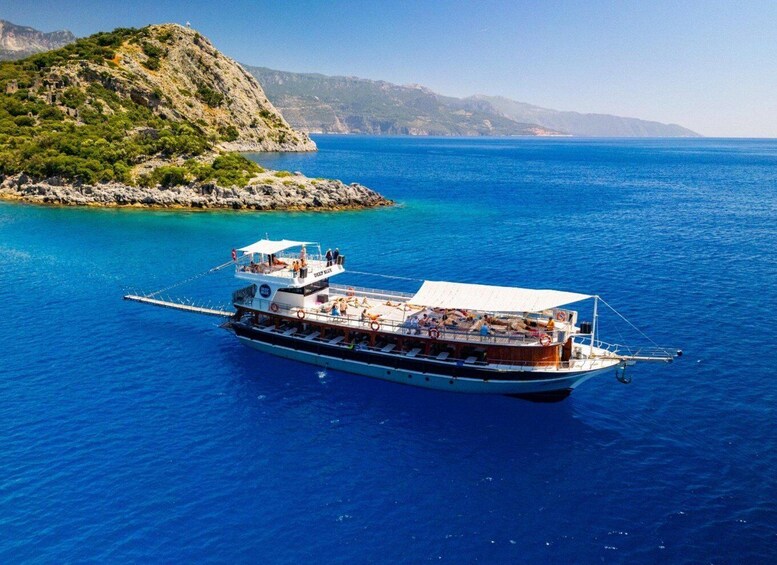 A boat with passengers on a clear blue sea, surrounded by rocky terrain and mountains. 1