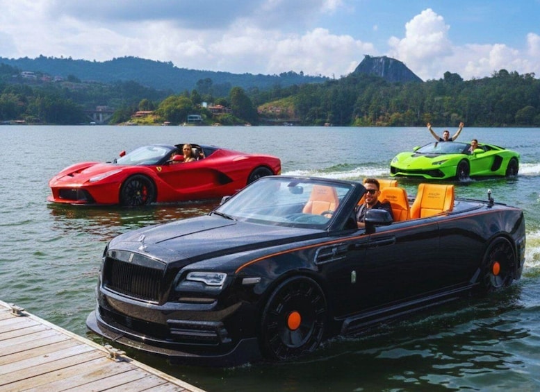 A luxury black convertible on a lake with a red sports car and a green sports car in the background. 2