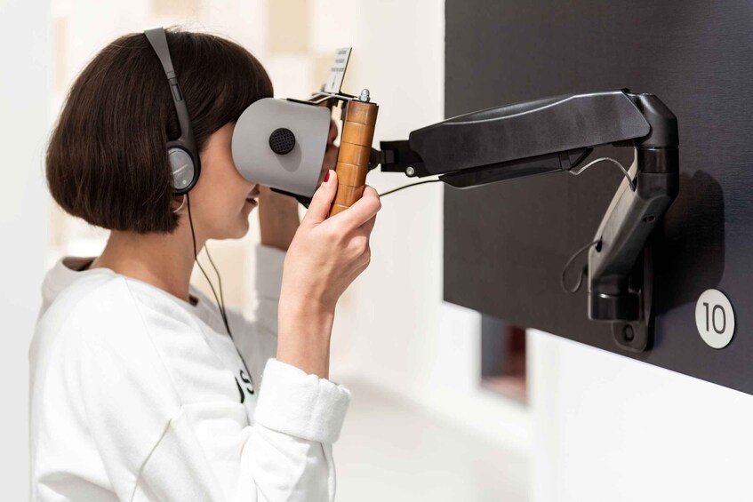 A person using a VR headset with a wooden handle, standing in front of a wall-mounted device with a number '10' visible. 5