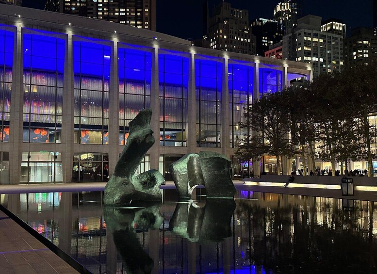A modern building with blue lighting and a reflective water feature with abstract sculptures. 2