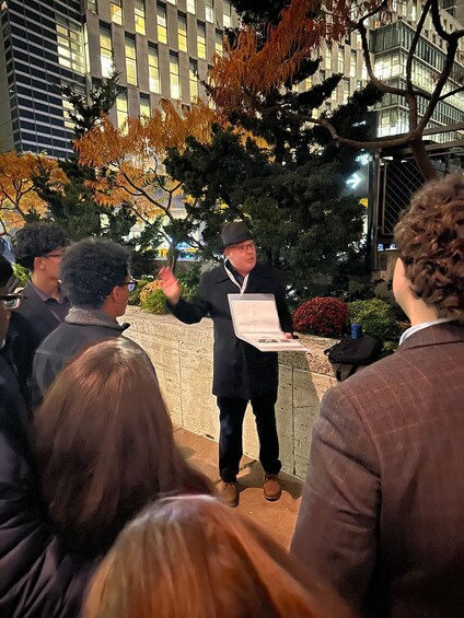 A person speaking to an audience outdoors at night with buildings in the background. 4